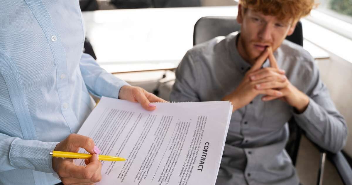 young man sitting at a desk as employer hold employee contract forms 